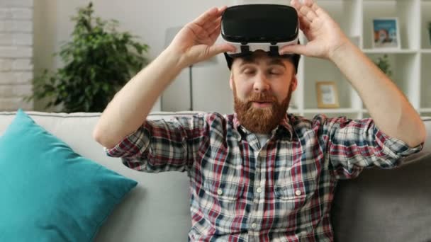 Mladí bokovky muž ve Vr headsetu sledovat 360 video doma při odpočinku na pohovce v obývacím pokoji než ji odpojit a usmíval se na kameru. Detailní záběr. — Stock video