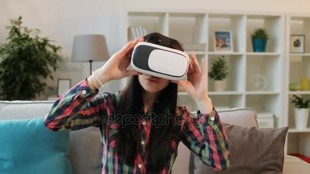 Junge Frau mit Kopfhörer schaut sich das 360-Video zu Hause an, während sie es sich auf dem Sofa im Wohnzimmer gemütlich macht. — Stockvideo