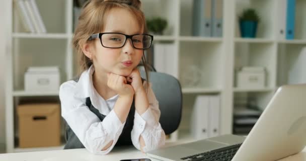 Caucasian girl siting on the desk in modern office. Young girl with glasses posing on the camera and smiling on office background. Close up. Indoor. — Stock Video