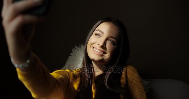 Mulher morena bonita levando selfie interior. Uma jovem bonita a fotografar-se em casa. A sorrir para a câmara. Rosto aparecendo da sombra — Vídeo de Stock