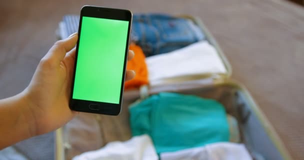 Close up woman hand holding smart phone with green screen on travel bag, suitcase blurred background. Preparing for a trip, vacation. Traveling. Chroma key — Stock Video