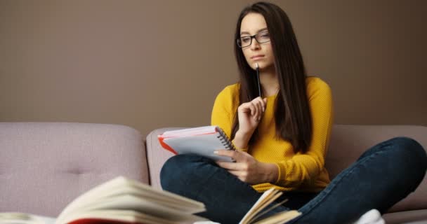 Bela menina estudante estudando em casa no sofá, lendo livros, observando, fazendo lição de casa. Movimento lento — Vídeo de Stock