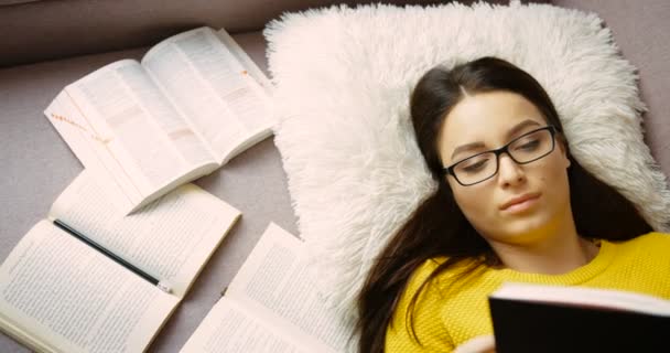 Joven estudiante estudiando, leyendo libros, haciendo la tarea mientras está acostado en el sofá en la sala de estar. De cerca. — Vídeo de stock