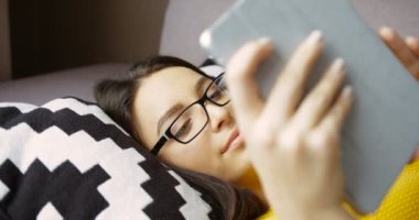 Çekici genç kadın kanepede yatan tablet cihaz kullanarak. Tablet bilgisayar ve güleryüzlü evde yazmadan gözlük güzel kadın. Yakın çekim