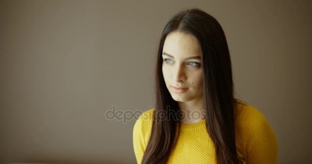 クローズ アップの肖像画。屋内のカメラ目線の美しい若い女性の肖像画を閉じます。黄色いセーターのきれいな女性。深刻な顔 — ストック動画