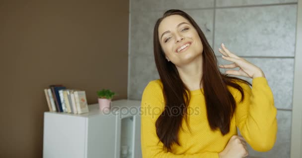 Potret wanita muda yang cantik tersenyum ke kamera di dalam ruangan. Wanita cantik dengan sweater kuning di ruang tamu. potret ditembak — Stok Video