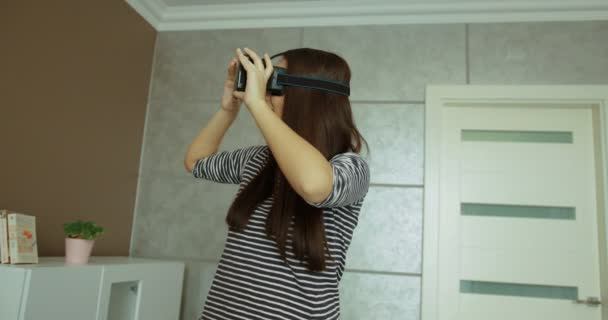 Красивая молодая женщина в VR гарнитуре смотрит на виртуальные объекты и трогает их в виртуальной реальности в гостиной у себя дома . — стоковое видео