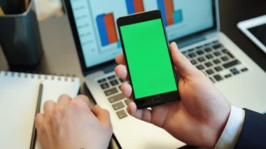 Diyagramları ile dizüstü kağıt üzerinde yeşil screan ile akıllı telefon kullanarak eller genç adam. Chroma anahtar. Dikey konumu.