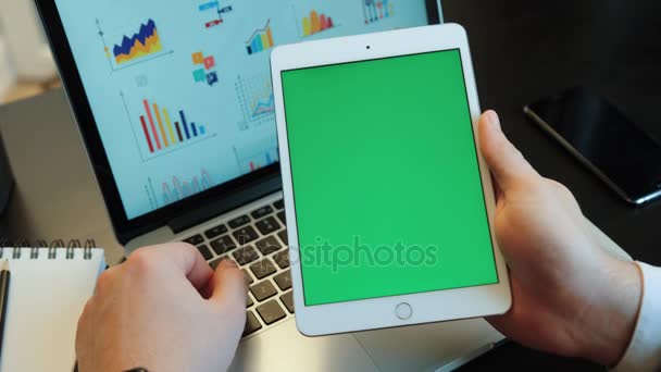 Giovani mani utilizzando tablet con screan verde sul backgroud portatile con diagrammi. Chiave cromatica. Posizione verticale . — Video Stock