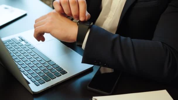 Close-up tiro de jovem homem de negócios em terno trabalhando duro usando laptop e relógio inteligente no fundo do escritório. Vista lateral . — Vídeo de Stock