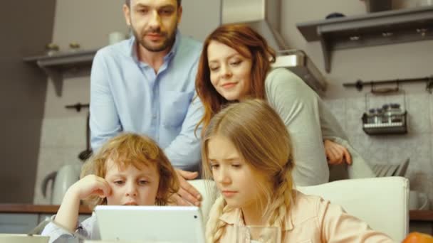 어린 소년과 소녀 부엌 디지털 노트북을 사용 하 여 노트북에서 뭔가 보여주는 그들의 부모에서 siting. — 비디오