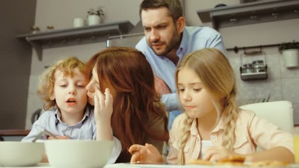 Familia teniendo un descanso rápido. Niño sentado en la madre y la niña comiendo en la cocina y el padre de pie junto a ellos . — Vídeos de Stock