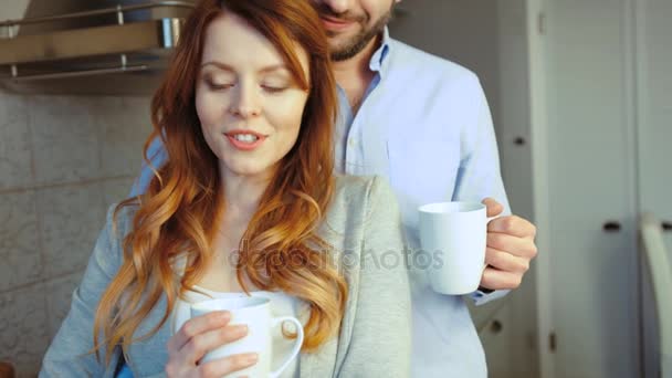 幸福的白种人夫妇的年轻女子和她的丈夫站在 kitcen 和喝咖啡。室内. — 图库视频影像
