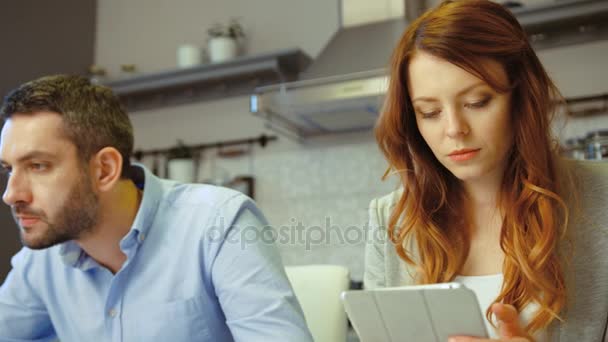 Mulher bonita jovem caucasiana com cabelo ruivo situado na cozinha com o marido usando tablet, sorrindo. Interior . — Vídeo de Stock