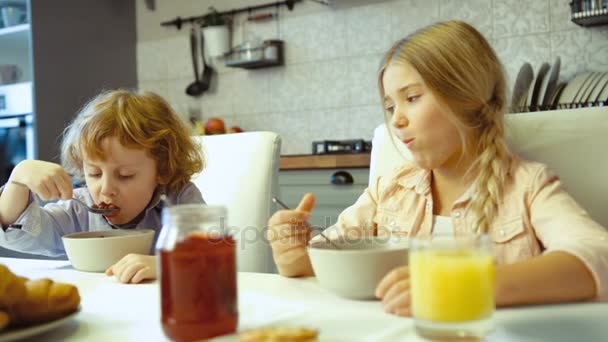 Niña y su hermano pequeño desayunando. Niños comiendo en la cocina. Niña y niño en la cocina. De interior . — Vídeos de Stock