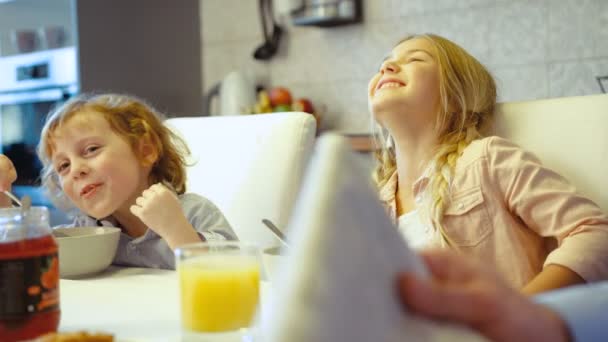 Λίγο καυκάσια παιδιά που τρώνε πρωινό σε λευκό τραπέζι. Νεαρό κορίτσι και ο αδελφός της χαμογελώντας χωροθέτηση στο τραπέζι στην κουζίνα. — Αρχείο Βίντεο