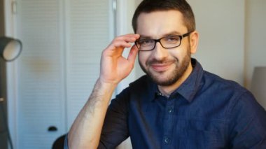 Gözlük kaldırma, kameraya bakıyor ve gülümseyen mavi gömlekli sakallı beyaz çekici adam portresi. Kapalı.