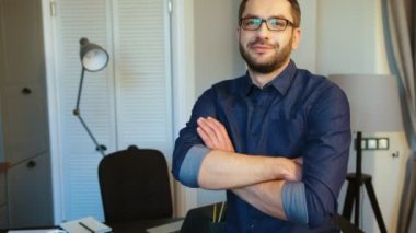 Eller beste, kameraya bakıyor ve gülümseyen mavi gömlekli sakallı genç beyaz güzel adam. Kapalı.