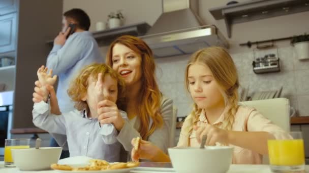 Caucasian attractive young woman with her children listening toi music using a digital tablet while her husband talking on mobile phone in kitchen. — Stock Video