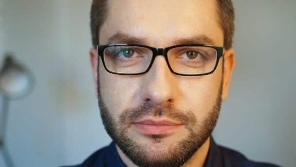 Bliska portret kaukaski atrakcyjny mężczyzna w okularach, z brodą, pozowanie na kamery poważnie i uśmiecha się. Wewnątrz. — Wideo stockowe