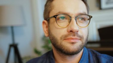 Kameraya bakarak ve gülümseyen mavi gömlekli sakallı bardaklarda beyaz çekici adam portresi. Kapalı.