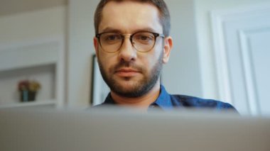 Ciddi beyaz genç adam gözlük kullanma laptop modern office mavi gömlekli sakallı portresi. Kapalı.