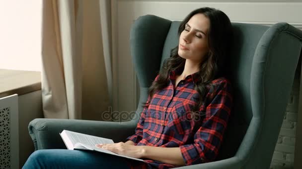 Atractiva joven siesta, durmiendo en una silla blanda. La mujer se echó una siesta mientras leía un libro sobre la sala de estar. De cerca. — Vídeo de stock