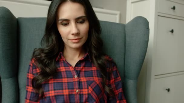 Mujer atractiva joven sentada en un sillón moderno y leyendo un libro interesante. De cerca. — Vídeo de stock