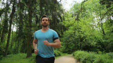 Yeşil parkta sabah koşu ve müzik kulaklık olan genç adam. Ağır çekim. Yakın çekim.