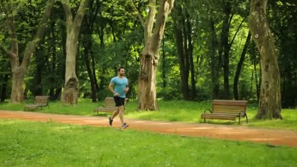 Giovane uomo in forma che corre nel parco al mattino. Un uomo che usa l'orologio intelligente. Rallentatore — Video Stock