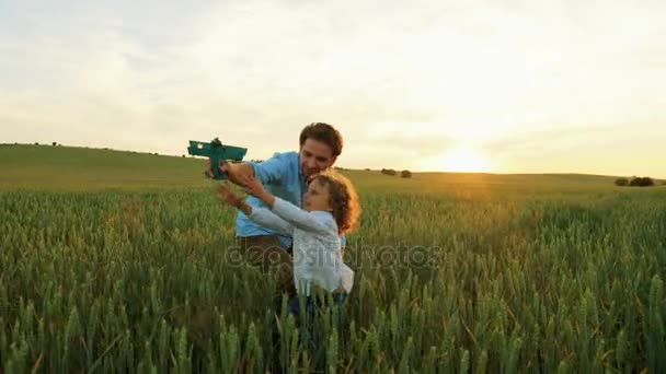 Glückliche Familie aus Vater und kleinem Sohn spielt mit blauem Holzflugzeug im grünen Weizenfeld bei Sonnenuntergang — Stockvideo