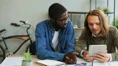Afrika ve beyaz iş adamı modern ofiste çalışmak için tablet kullanma.