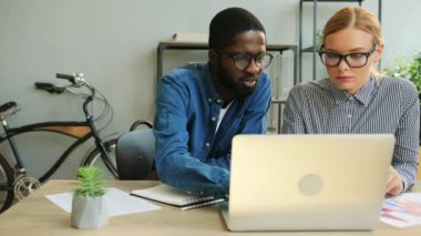 Afrika genç iş adamı ve beyaz sarı saçlı iş kadını ile birlikte modern ofis dizüstü kullanarak Finans raporu üzerinde çalışan gözlük.