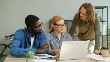 Beyaz Sarı saçlı iş kadını ofiste laptop beyaz ve Afrika adama onun finans rapor gösterme.