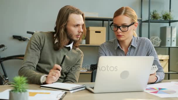 Hombre de negocios con cabello largo y mujer de negocios en las gafas que trabajan en la oficina utilizando el ordenador portátil . — Vídeo de stock