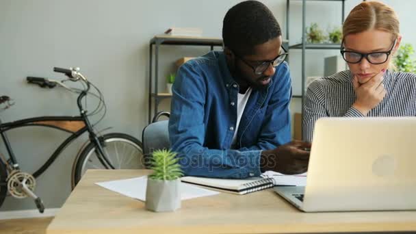 Afrikanska affärsman och kaukasiska blonda hår affärskvinna arbetar tillsammans på kontoret använder laptop. — Stockvideo