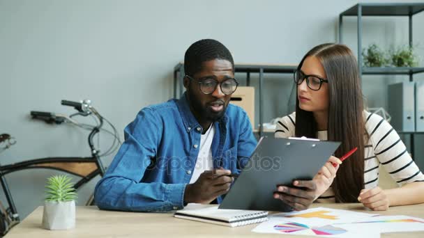 Hombre de negocios africano y mujer de negocios caucásica en las gafas trabajando juntos en la oficina en el proyecto internacional global . — Vídeos de Stock