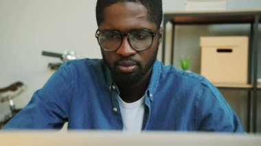 Afrika genç iş adamı modern ofis yeni Finans rapor içinde belgili tanımlık laptop üzerinde mavi kot gömlekli gözlüklü görüntüsünü kapatmak.