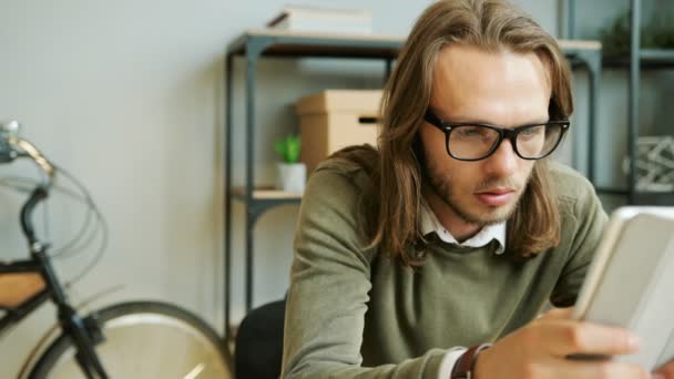Retrato del joven hombre de negocios caucásico con gafas trabajando en la tableta en la nueva startup en la oficina moderna . — Vídeo de stock