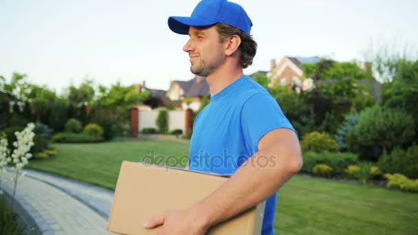 Feche o retrato do correio que anda com o cartão à casa para entregar o pacote à mulher feliz . — Vídeo de Stock