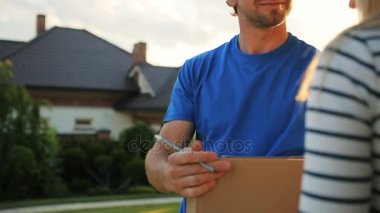 Genç kurye karton ev, mutlu bir kadın paket alma ve bu almak için belgelerin imzalanması için teslim etmek. Atış kapatın.