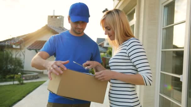 Porträt einer kaukasischen jungen Frau, die die Dokumente für die Paketannahme beim Kurier unterschreibt, sich der Kamera zuwendet und lächelt. — Stockvideo