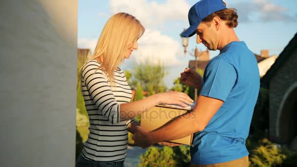 Jolie jeune femme signant les documents pour obtenir le paquet du courrier sur le fond du jardin. Vue du bas . — Video