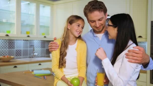 笑顔に幸せな若い白人家族とキッチンのカメラに possing。男は妻と娘を抱き締めると、笑みを浮かべて. — ストック動画