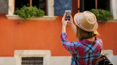 Genç şık kadın güzel binanın eski şehirde akıllı telefon kullanarak fotoğraf yapma. Arkadan görüntülemek.