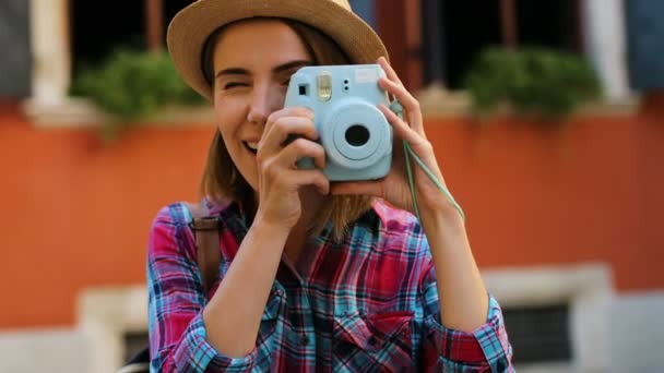 Красавица в шляпе фотографирует на фоне оранжевой стены стильную голубую камеру. Закрыть . — стоковое видео