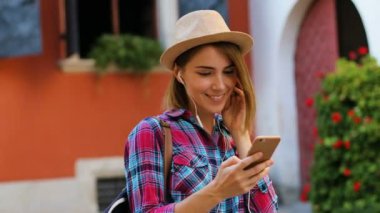 Güzel genç kadın moda şapka şehirde smartphone kullanarak kulaklık müzik dinleme.