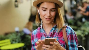 Güzel genç kadın moda portre smartphone kullanarak arkadaşlarınızla sohbet, aile içinde şehir için kulaklık müzik dinleme şapka.