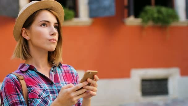 Mujer guapa en el sombrero charlando con amigos usando un teléfono inteligente en la calle de la ciudad. Vista lateral . — Vídeos de Stock