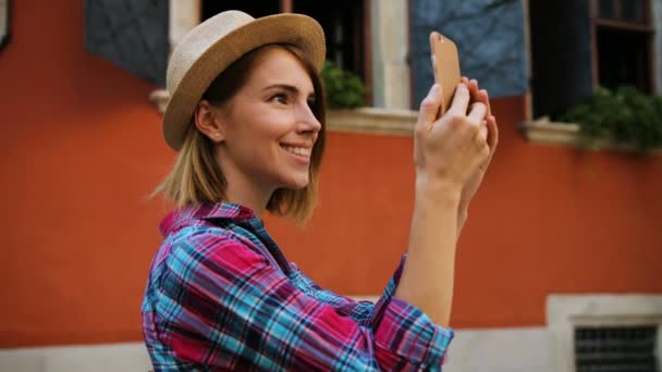 年轻快乐时尚的女人的美丽建筑在古老的城市使用智能手机的照片制作。查看从侧面. — 图库视频影像